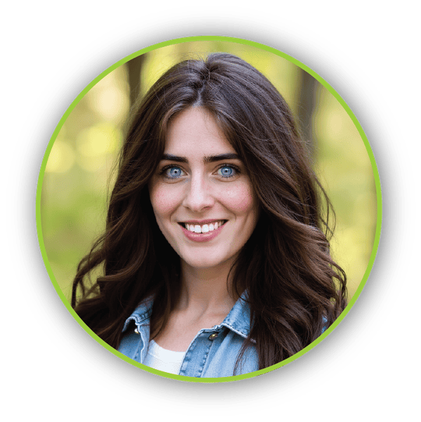 Kaela_Motschenbacher Kaela Motschenbacher – Smiling woman with long brown hair in a denim jacket, standing outside in a sunlit forest.